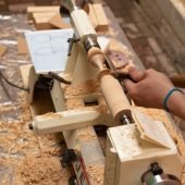 Wood lathe shaping a wooden object, close-up of shavings and gouge